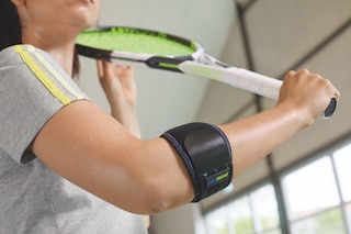 Close up of woman playing tennis at indoor gym, wearing and Actimove Sports Edition Elbow Strap with Hot/Cold Pack 
