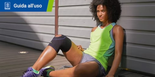 Una donna in abbigliamento sportivo con una ginocchiera riposa appoggiata a una parete