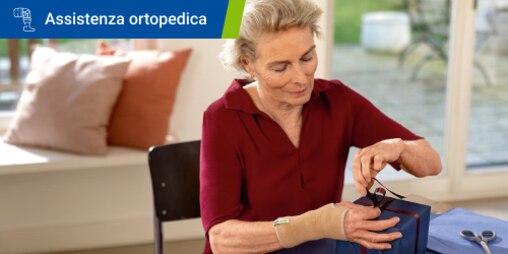 Una donna anziana con un polsino avvolge un nastro attorno a regalo su un tavolo