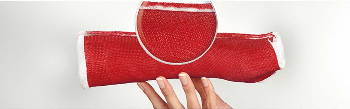 A hand holding a red cast tape against a white background