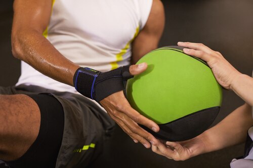Close-up of man wearing Actimove Sports Edition Thumb Stabilizer while holding a green ball at the gym
