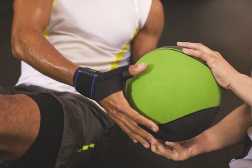 Close-up of man wearing Actimove Sports Edition Thumb Stabilizer while holding a green ball at the gym
