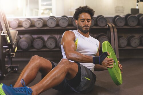 Man wearing Actimove Sports Edition Thumb Stabilizer while lifting weights at the gym
