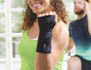 Zbliżenie na kobietę noszącą ortezę stabilizującą nadgarstek Actimove Sports Edition na ręce podczas treningu na siłowni
