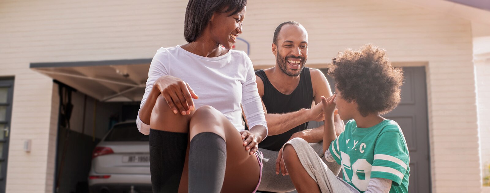 A woman wearing JOBST Sport compression socks sits with her family, smiling and enjoying time together outside their home.