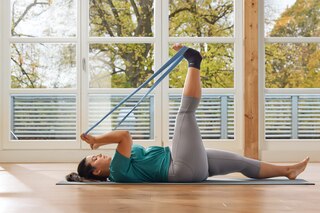 Egy nő éppen a lábát nyújtja a konditeremben egy matracon, Actimove Sport Plus méretű bokatámaszt viselve

