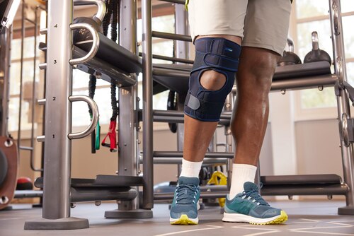 Close up of man working out at gym, wearing Actimove Sports Edition Knee Brace Wrap Around with Polycentric Hinges and Condyle Pads
