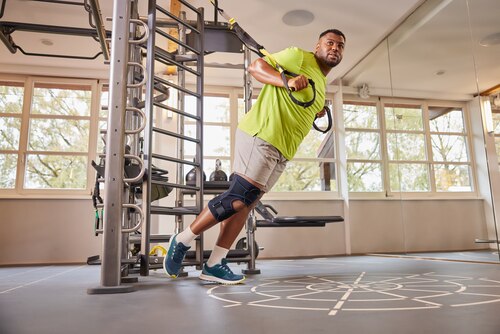 Man working out at gym, wearing Actimove Sports Edition Knee Brace Wrap Around with Polycentric Hinges and Condyle Pads
