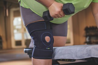 Närbild på kvinna på gym som lyfter vikter och bär Actimove Sports Edition justerbart knästöd i plusstorlek
