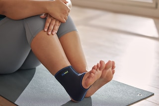 Közeli kép egy nőről, aki a lábát nyújtja az edzőteremben, és Actimove Sport Plus méretű bokatámaszt visel
