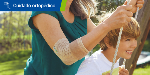 Mujer empuja a un niño en un columpio mientras usa la codera Actimove Everyday Supports porque tiene epicondilitis. Se lee el texto “Cuidado ortopédicos” en un recuadro.