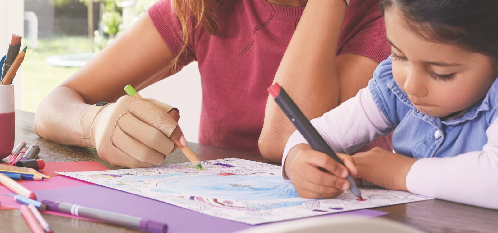Mujer usando guantes para la artritis de Actimove para aliviar la artritis psoriásica, coloreando con una niña pequeña.