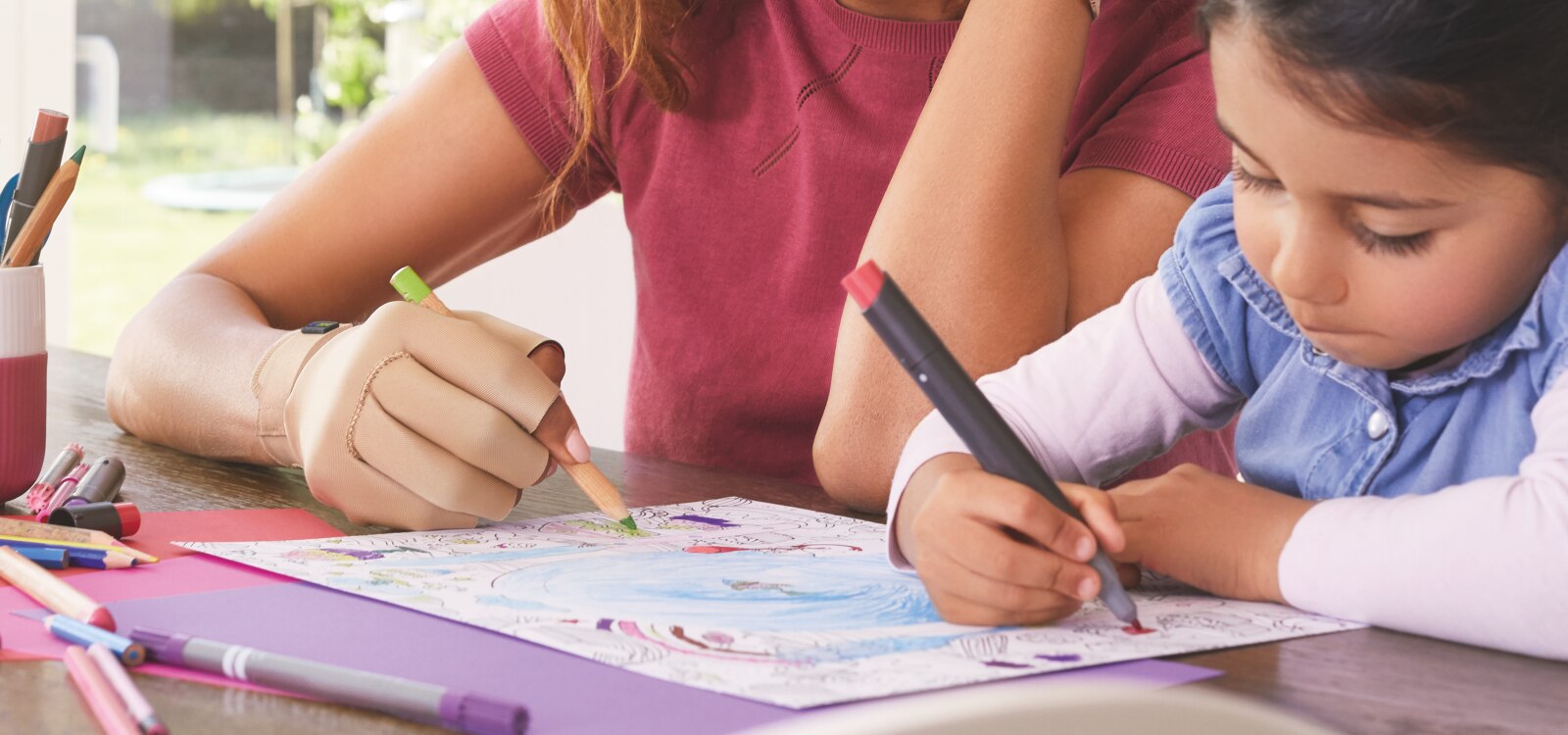 Mujer usando guantes para la artritis de Actimove para aliviar la artritis psoriásica, coloreando con una niña pequeña.