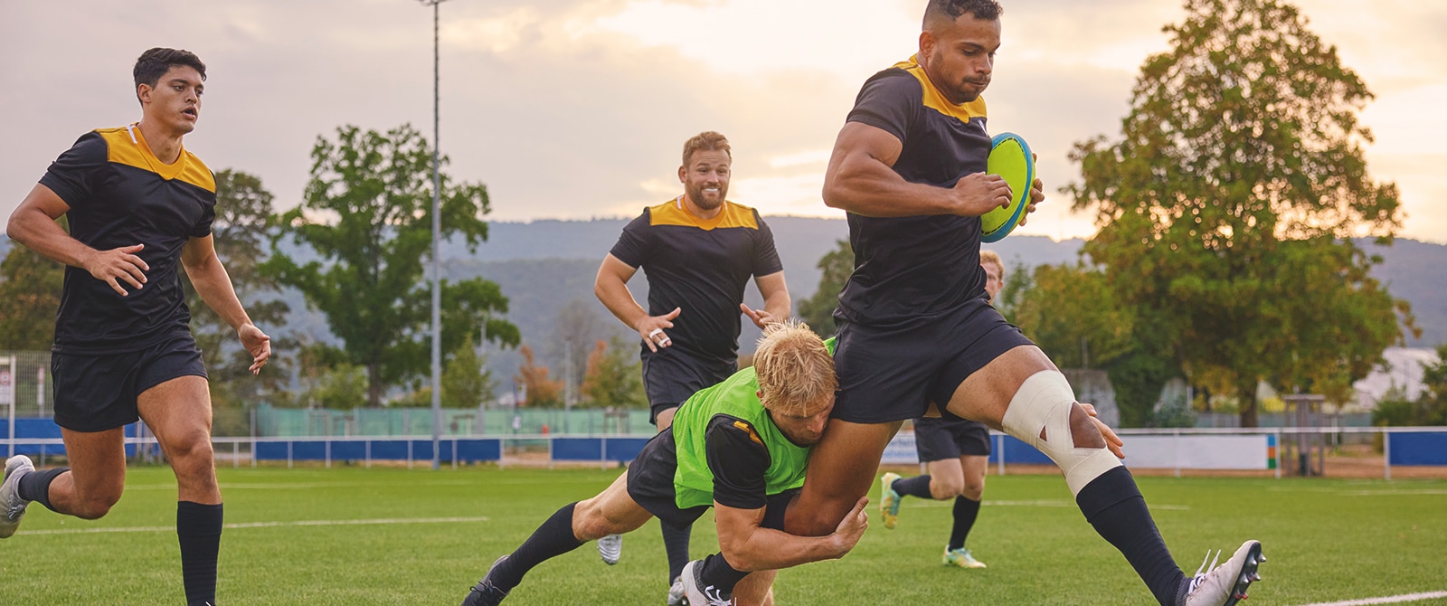 Un jugador de rugby que lleva cinta deportiva en la rodilla es placado por otro jugador.