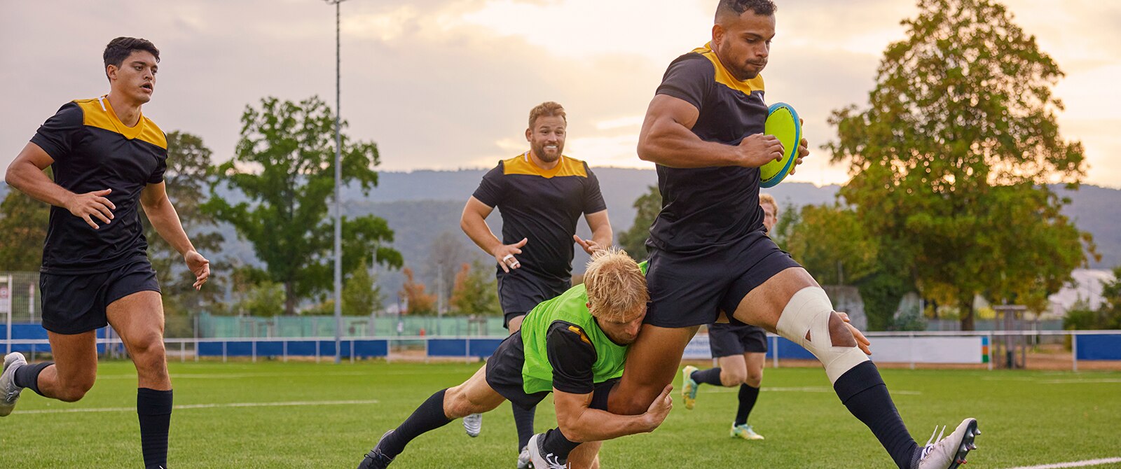 A rugby player wearing sports tape on his knee is tackled by another player.