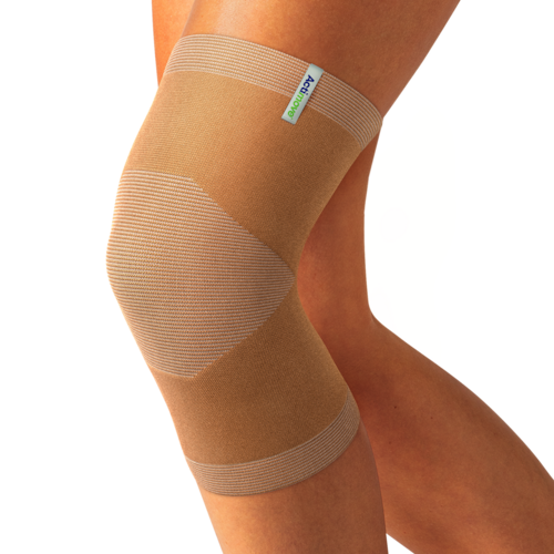 Beige knitted Actimove Arthritis Care Knee Support with heat reflecting technology on slightly bent knee 
