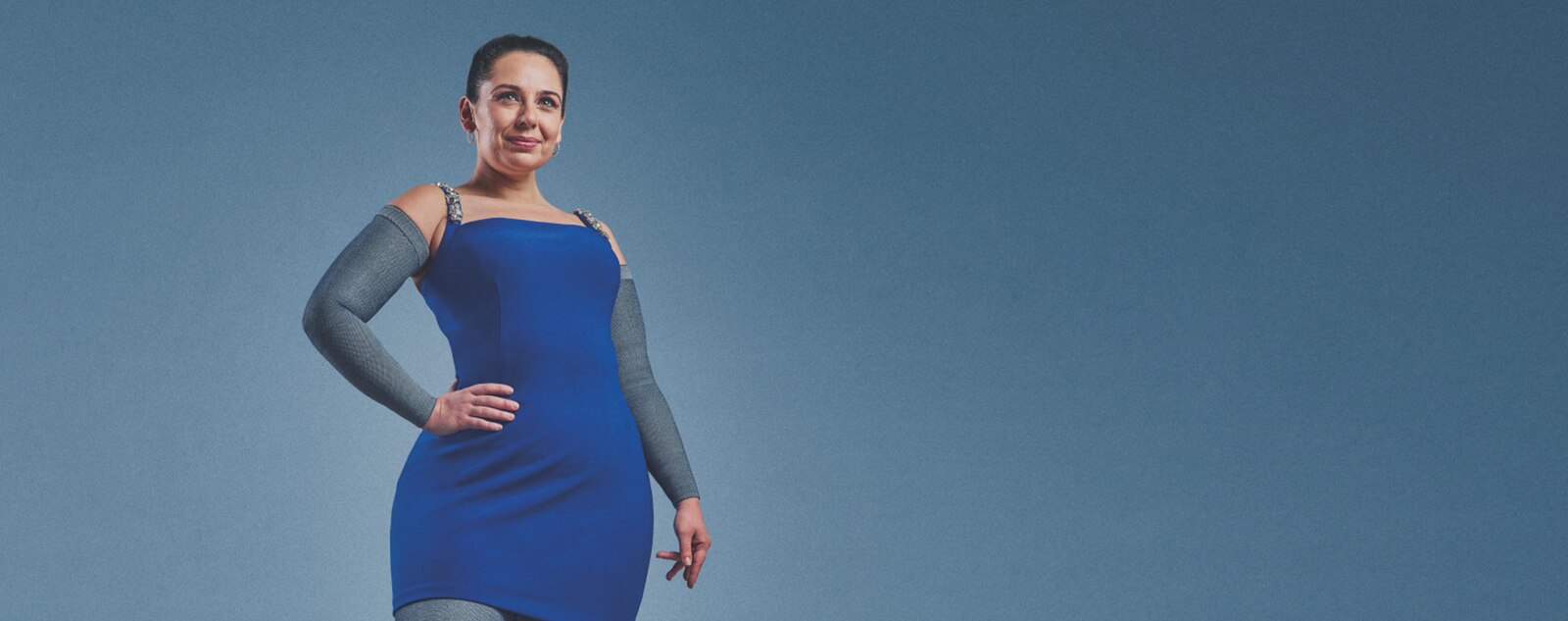 Smiling woman wearing a blue dress and JOBST® Confidence compression sleeves.