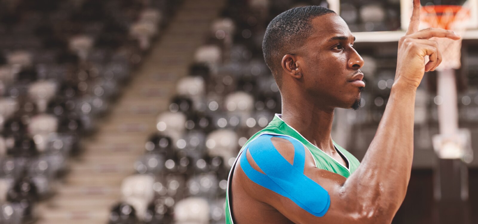 Een basketballer gebruikt blauwe kinesiotape op zijn schouder tijdens een wedstrijd.