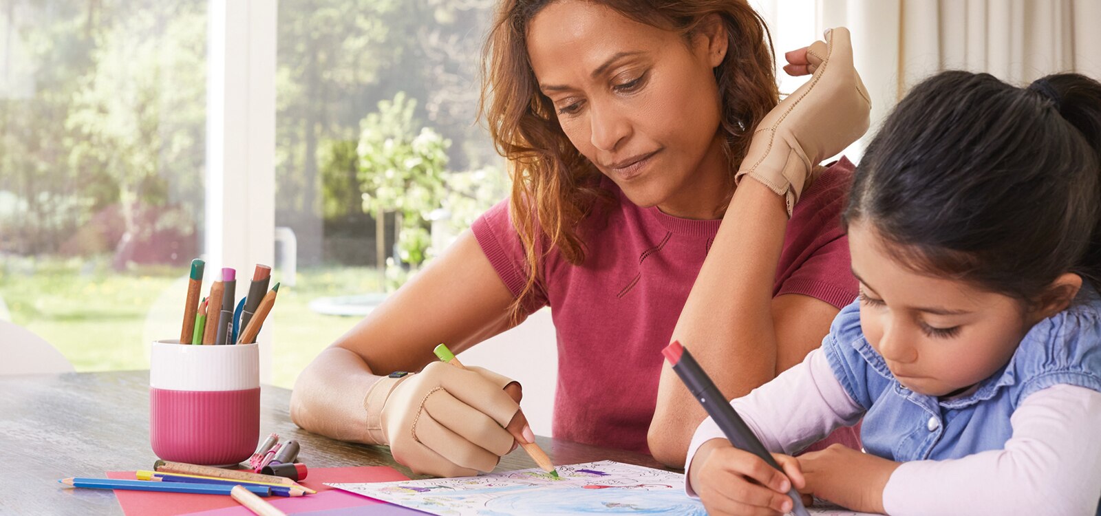 Matka z córką siedzą przy stole, kolorując rysunek