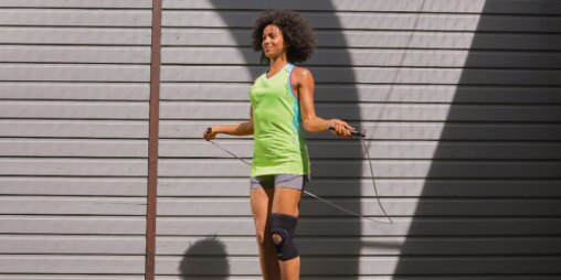 Woman wearing exercise clothes and a knee support uses a jump rope outside.