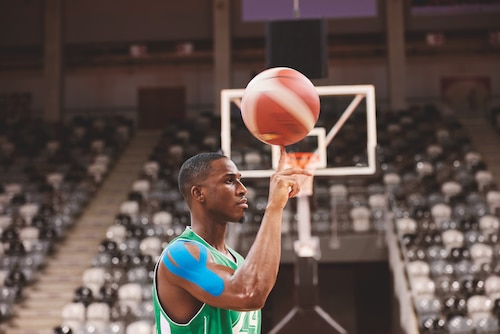 A basketball player in a green jersey holding a basketball, wearing Leukotape k kinesiology tape.