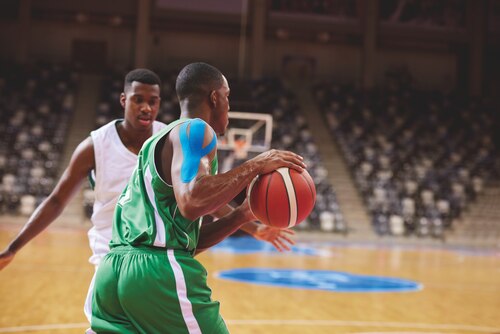 Two basketball players engaged in a game, one wearing Leukotape K kinesiology tape on his arm