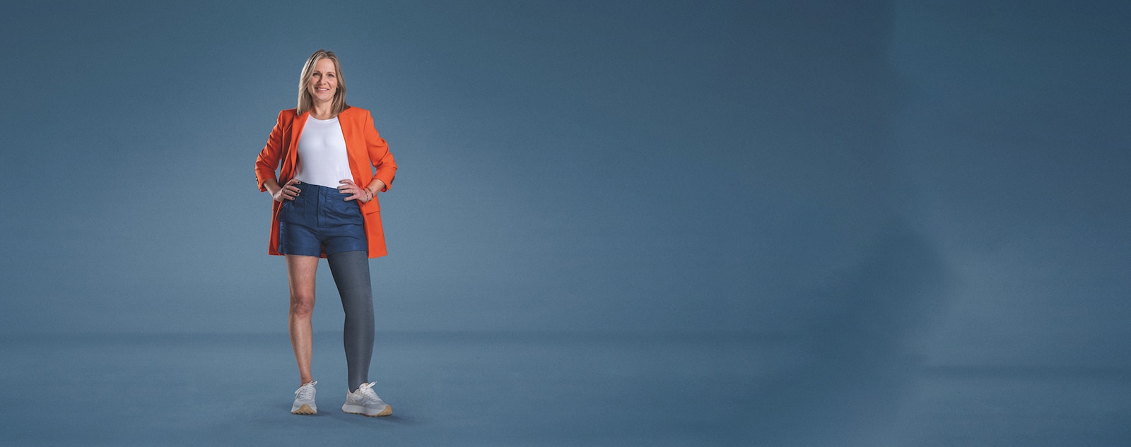 Une femme souriante, vêtue d’un blazer orange et d’un short foncé, portant Confiance de JOBST